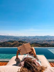 a woman laying on a bed reading a book at Chalet nas Nuvens with Infinity Pool in São Bento do Sapucaí