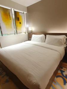 Elle comprend un grand lit blanc avec deux oreillers et deux fenêtres. dans l'établissement Novotel Manila Residence Hotel by Jolly Luxe Suites at Acqua, à Manille