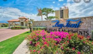 a sign at the entrance of a resort with flowers at CASA PORS Beach Front Apartment with security, pool &jacuzzi BAYFRONT in Portmore