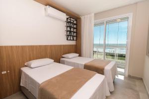 two beds in a room with a large window at Edifício Solar do Atlântico Beira Mar de Bombas in Bombinhas +224 photos