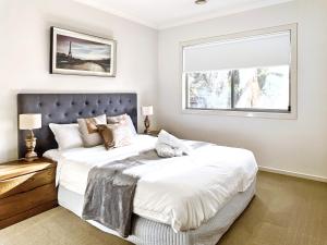 Un dormitorio con una gran cama blanca con ventana. en Modern Golfside Retreat, en Carrum Downs