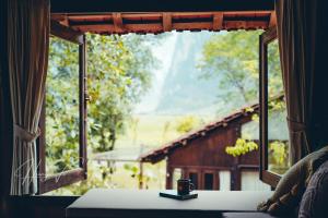 a window with a coffee cup on a table looking out at a barn at Đến Nơi Có Gió - Homestay And Coffee in Hữu Lũng