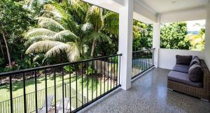 a balcony with a couch and palm trees at Cowrie Beach House Port Douglas in Port Douglas