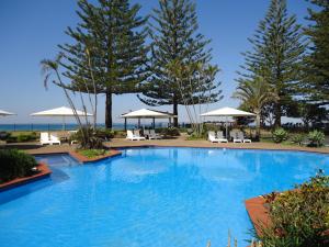 a large blue swimming pool with chairs and umbrellas at Absolute Beachfront Family Villa in Kororo Basin