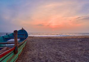 a boat sitting on the beach at sunset at Alleppey Holiday Beach Resort by VOYE HOMES , Sea View with Direct Beach Access in Alleppey