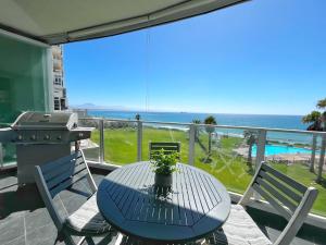 een tafel en stoelen op een balkon met een grill en de oceaan bij Coastal Hospitality - Beach Club 205 in Mosselbaai