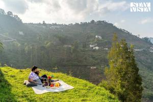 a person sitting on a picnic blanket on a hill at StayVista at Kurinji Amaze Kodai with WiFI & Heater in Kodaikānāl
