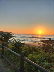 a sunset on the beach with a fence at Smooth Sailing Unit -Ebbtide Beach House in Port Shepstone +10 photos