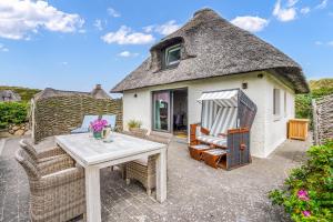 a house with a thatched roof with a table and chairs at Strandhaus in Hörnum
