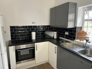 a kitchen with white cabinets and black tile on the wall at Ty Abertawe in Cockett