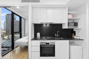 a kitchen with white cabinets and a stove top oven at Minimalist Studio Escape 31506-2 in Brisbane
