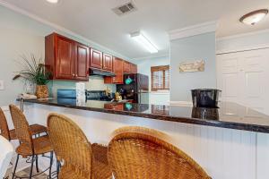 a kitchen with wooden cabinets and a bar with chairs at Romar Beach 205 in Gulf Shores