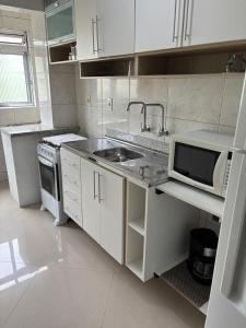 une cuisine blanche avec un évier et un micro-ondes dans l'établissement Prático e Aconchegante, à Porto Alegre