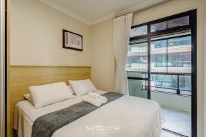 a bedroom with a bed and a large window at Apto c varanda e churrasq em cond beira mar UAR301 in Itapema