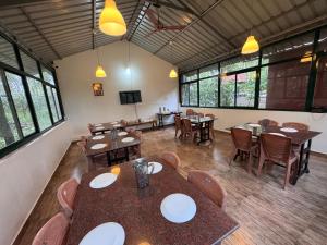 une salle à manger avec tables, chaises et fenêtres dans l'établissement Manuvan home stay ac cottage, à Kushalanagar