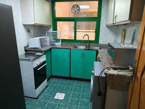 cocina con armarios verdes, fregadero y ventana en Modern Comfort Stay, en Sharjah