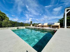 a swimming pool with two chairs and a table on a patio at Villa Les Oliviers - Élégance & Sérénité in Les Terres Basses