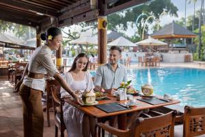 a group of people sitting at a table near a pool at Mana Suites Bali in Kuta