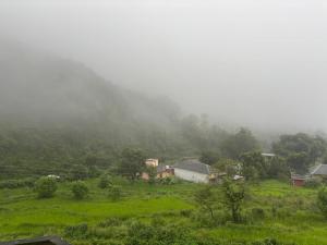 Un campo brumoso con casas en medio de una montaña en Serene Stay Baijnath, en Sahel