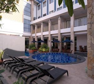 a hotel with a pool with lounge chairs and umbrellas at Vrata Hotel Yogyakarta in Kalasan