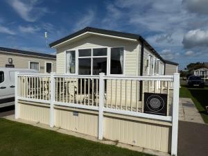 a small house with a white fence and a porch at Palm Grove 181- Golden Palm - Pet friendly, WiFi, central heating, bed linen - Meadow Lakes Caravan & Lodge Hire in Chapel Saint Leonards