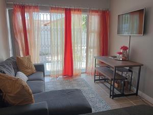 a living room with a couch and a table and red curtains at The Sands Ground-floor apartment in Blouberg in Cape Town