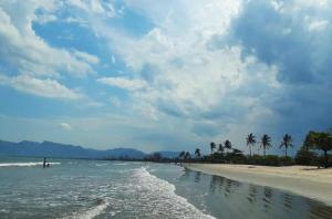 einen Strand mit Palmen und dem Meer an einem wolkigen Tag in der Unterkunft Seu lar na Praia, Condomínio Vila Gustavo-excelente localização in Caraguatatuba