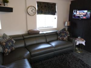 a leather couch in a living room with a clock at Hamlet Cottage sleeps 3-4 Stratford upon Avon in Stratford-upon-Avon