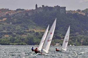 three people on sailboats in the water with a castle in the background at Peter giardino e casa sul lago in Bracciano