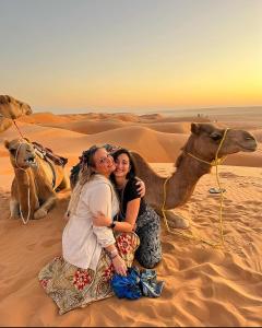 Al RakaにあるModern private bedouin campのラクダと一緒に砂漠に座っている二人の女性