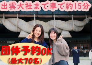 出云市Villa Izumoya的两名妇女站在一座建筑物前面,有标志