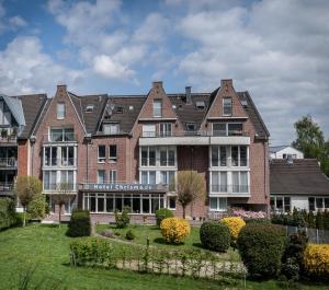 ein großes Backsteingebäude mit einem Garten davor in der Unterkunft Hotel Chrisma in Düsseldorf