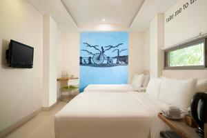 a hotel room with a bed, television and a painting on the wall at Grandmas Plus Hotel Legian in Legian