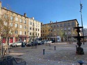 eine Stadtstraße mit Gebäuden und einem Brunnen in der Mitte in der Unterkunft Le Savoyard in Saint Etienne