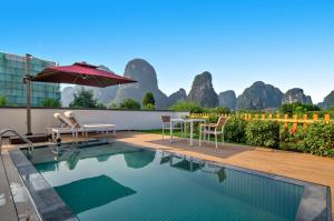 a swimming pool with an umbrella and a table and chairs at 桂林阳朔良宿 LS Hotel Liangsu Yangshuo in Gaotian