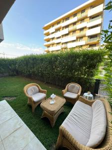 eine Terrasse mit Korbstühlen und Tischen sowie ein Gebäude in der Unterkunft Cozy Garden Flat with Full Kitchen in Madīnat aţ Ţalāʼi‘