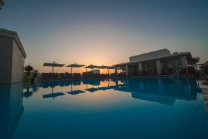 a swimming pool with chairs and umbrellas in the sunset at Maritim Antonine Hotel & Spa in Mellieħa