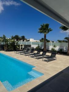 - une piscine avec des chaises et un palmier dans l'établissement Villa Ashdene - luxury modern villa with large heated pool wifi uk tv bar & BBQ, à Playa Blanca