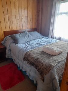 a bed with a pillow on it with a window at Cabañas almendra in Quellón