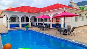 a house with a pool and tables and umbrellas at The Gambian Princess in Sukuta
