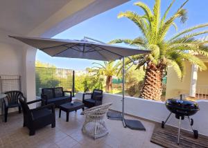 a patio with chairs and an umbrella and a palm tree at Aldeamento Praia dos Beijinhos in Porches