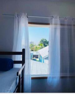 Schlafzimmer mit einem Bett und einem Fenster mit weißen Vorhängen in der Unterkunft Pousada Lume Beach House Peruíbe in Peruíbe