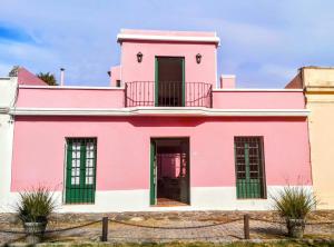 ein rosafarbenes Gebäude mit grünen Türen und einem Balkon in der Unterkunft La Casa Rosada del Barrio Histórico in Colonia del Sacramento
