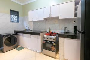 a kitchen with white cabinets and a stove and a dishwasher at Equinox Vacation Apartments in Bulambiro