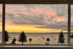 Una vista de una puesta de sol desde una ventana con barcos en el agua. en Panorama Penthouse Luxe Ocean Views & Pool, en Mount Maunganui