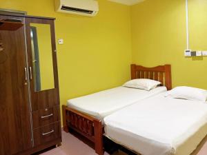 two beds in a bedroom with yellow walls and a cabinet at Hotel Rembau in Rembau