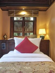 a bed with two red pillows and a window at Ancient Huế Garden Houses in Hue