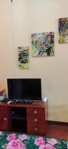a room with a tv on a dresser with paintings on the wall at Purnama Homestay in Kampong Bukit Badong