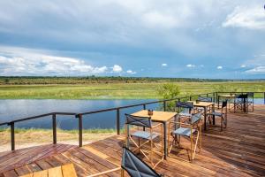 a deck with tables and chairs next to a body of water at Chobe River Camp in Ngoma