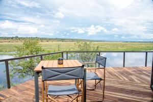 a table and two chairs on a wooden deck with water at Chobe River Camp in Ngoma